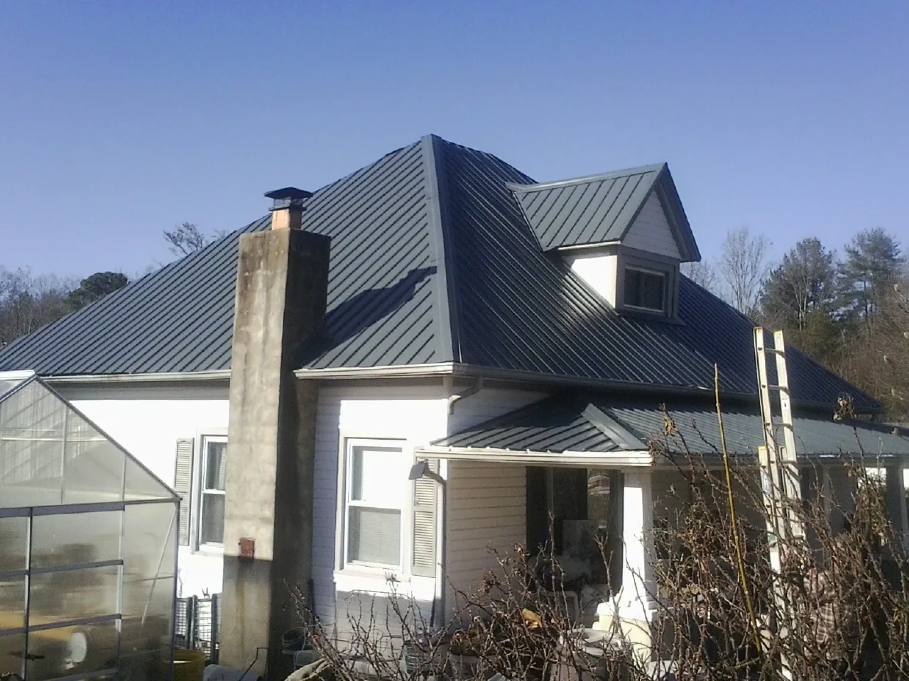 Dark blue standing seam metal roof on a white farmhouse with dormer — Slate & Tile Roof Repair by Roofing Brothers in West Sunbury