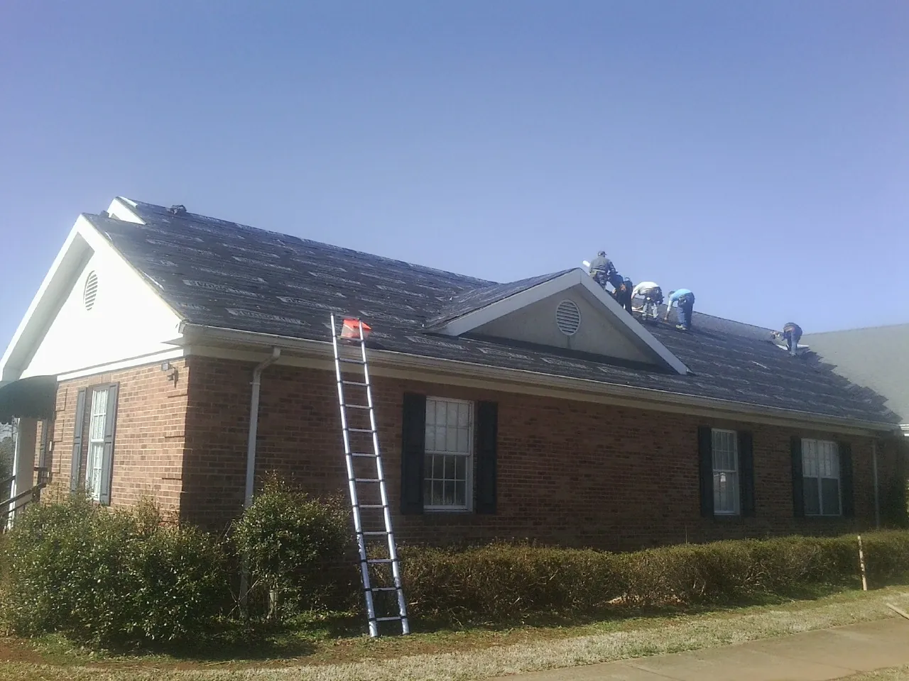 Crew tearing shingles off a brick ranch roof with a ladder set — Emergency Roof Repair work by our crew in West Sunbury