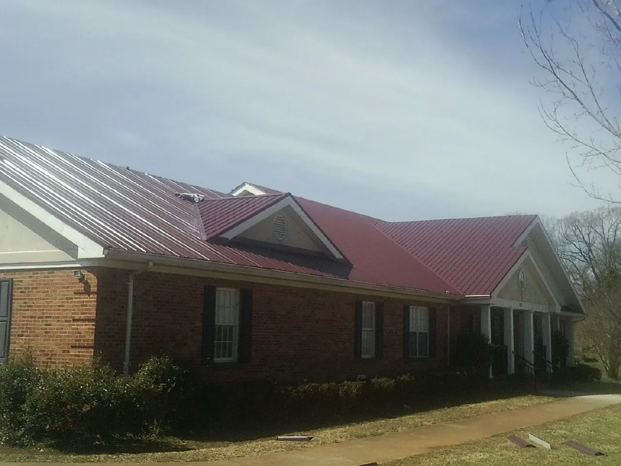 Red metal roof with gabled entries on a long brick building, from a Hail Damage Roof Repair job in West Sunbury