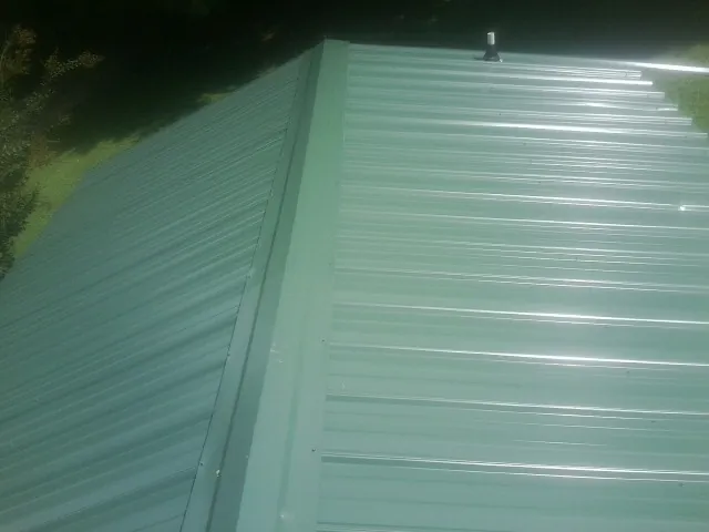 New green metal panels meeting at the ridge of a roof — Flat Roof Repair work by our crew in West Sunbury