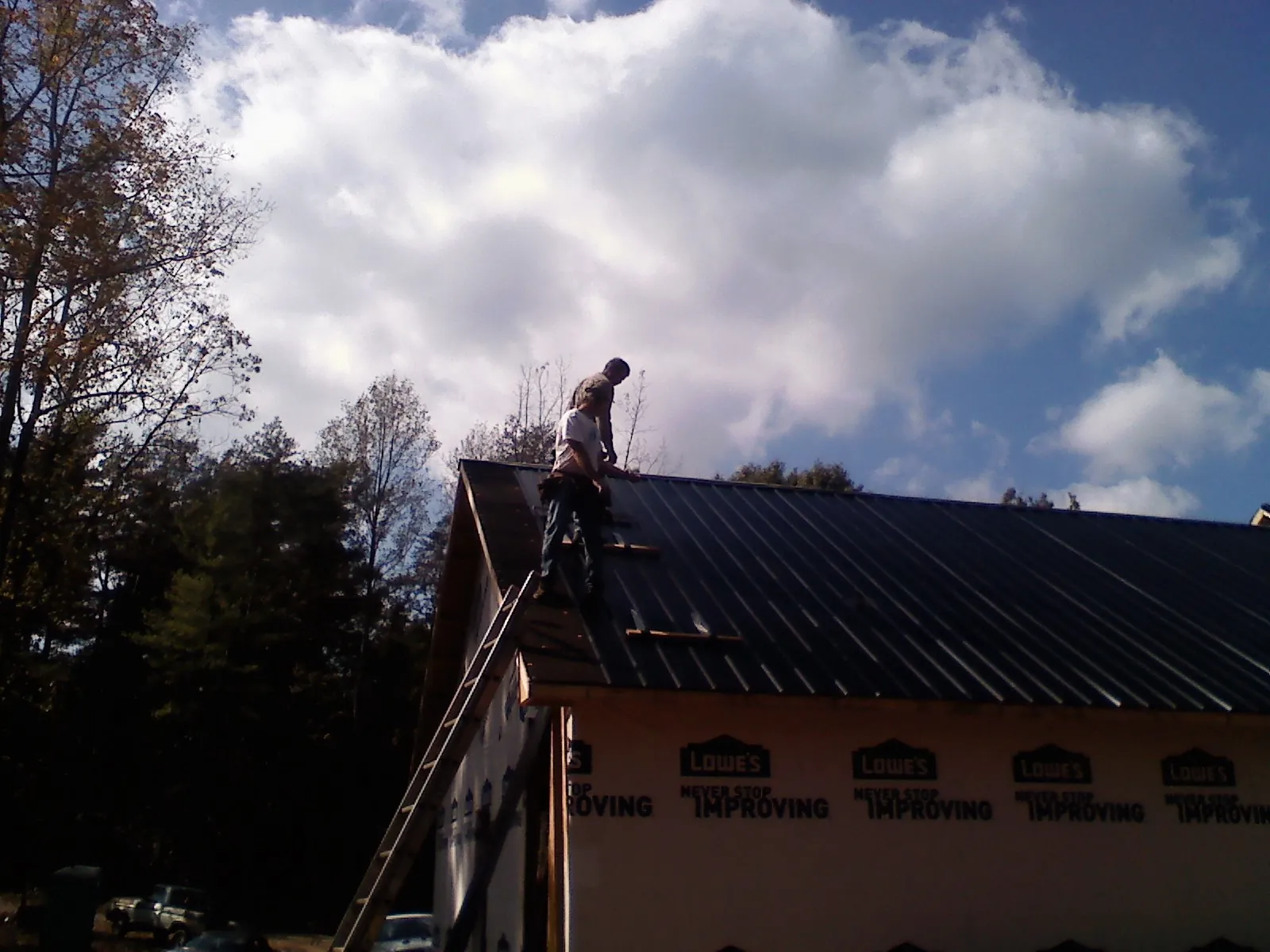 Roofer fastening dark metal panels high against a cloudy sky, from a Roof Inspection job in West Sunbury