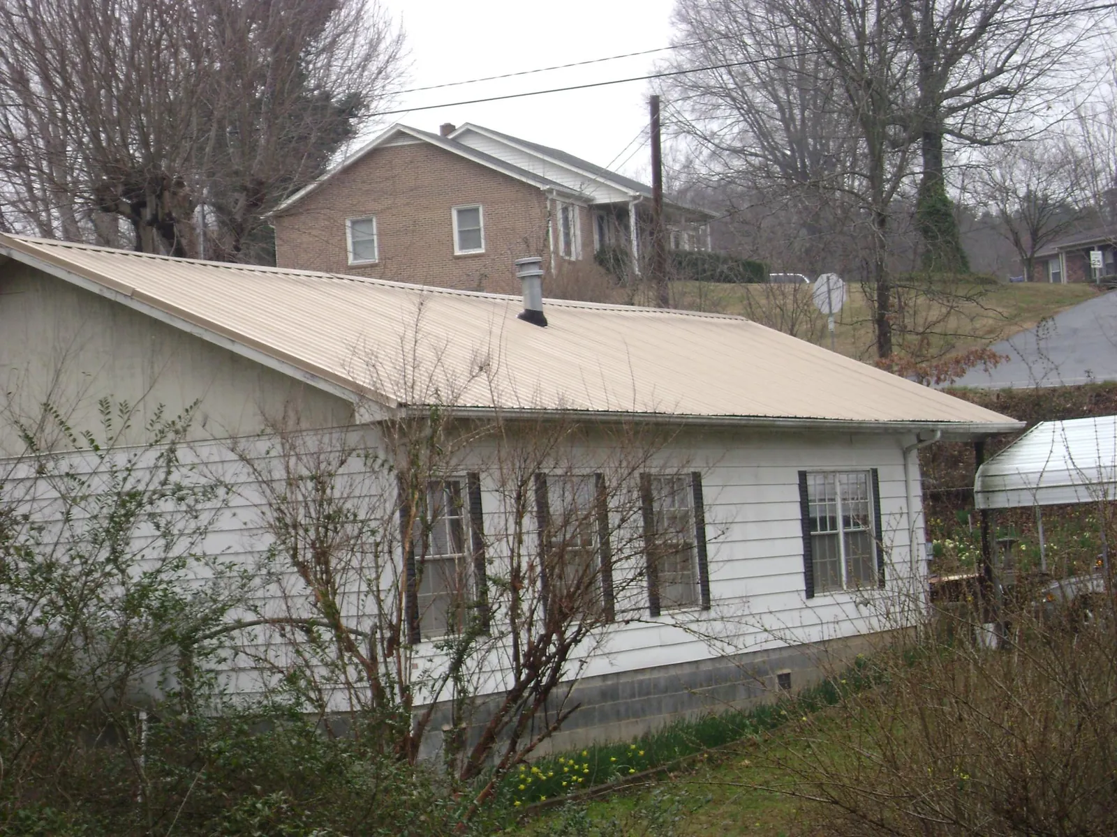 Tan metal roof on a white sided house set into a hillside — Commercial Roofing by Roofing Brothers in West Sunbury